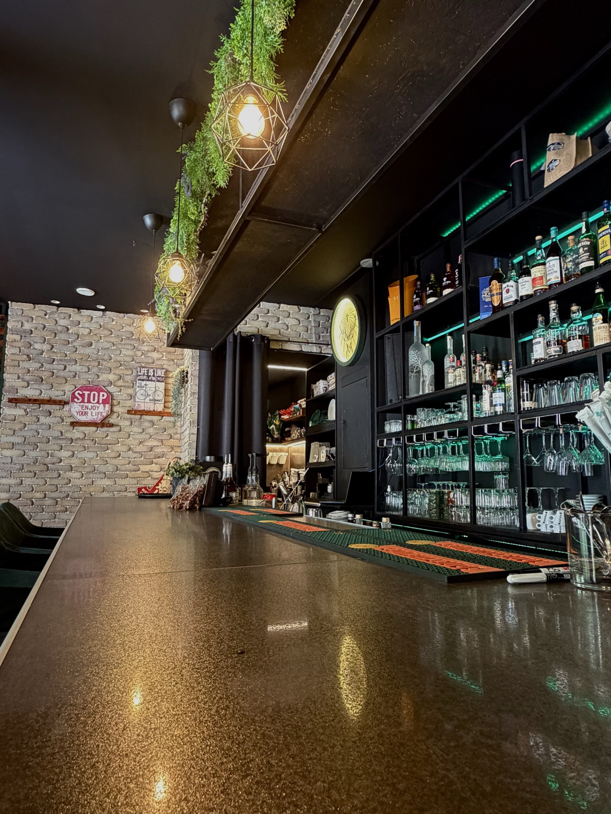 Along the polished bar counter — brick, bottles and pendant light